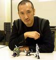 A photograph of Kaneko with the three main figures he designed for Shin Megami Tensei Card Game: Nocturne Ver. Part 2